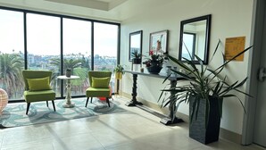 A modern room with large windows, two green chairs, a small table, and a potted plant. - Private Cozy Spacious Condo Unit with Gym— Walk distance to market (Los Angeles)