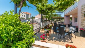Un patio al aire libre con una mesa y sillas, rodeado de plantas en macetas y una valla de metal.