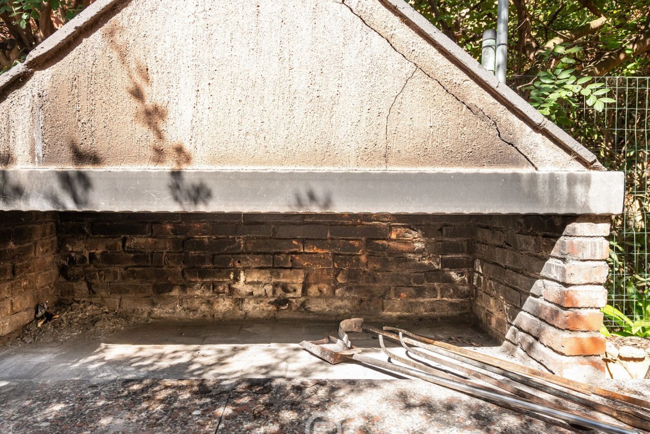 Une structure en briques dotée d’un toit en béton, entourée d’un mur de briques et de divers matériaux de construction disposés au sol.