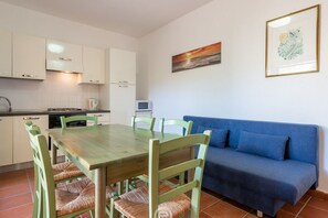 A compact living space with a dining area, kitchenette, and a blue sofa. - Coastal Apartments - Comfort (Cabras)