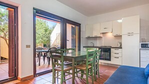 Uma cozinha compacta com armários brancos, uma mesa de jantar com cadeiras e uma porta de vidro deslizante para uma área externa.