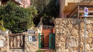 Escadaria de pedra que leva à entrada de um prédio, placa de proibido estacionar e vaga de estacionamento para deficientes.