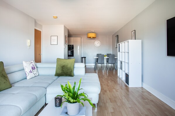 A modern living room with a light blue sofa, a coffee table with a plant, and a dining area with chairs and a table.