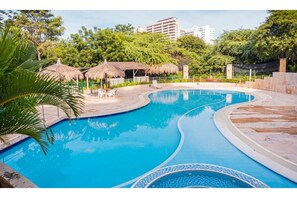 Relax by the resort pool surrounded by lush greenery and thatched umbrellas.