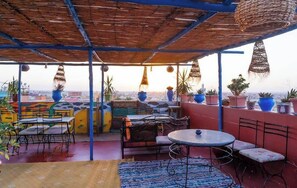 An outdoor patio with tables and chairs, potted plants, and a view of the cityscape. - Dar Merzouga Meknes (Meknes)