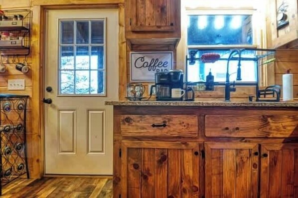 Une cuisine rustique avec des meubles en bois, un panneau indiquant « café » et une fenêtre donnant sur un paysage enneigé.