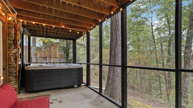 Een overdekt terras met een hottub, stenen muren en grote ramen met uitzicht op een bos.