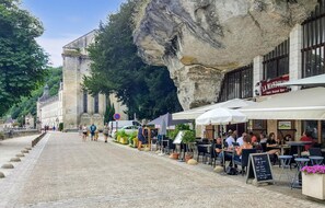 Eine Kopfsteinpflasterstraße gesäumt von Straßencafés, ein historisches Gebäude und eine Klippe.