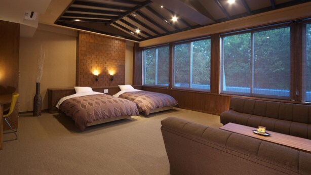 Een kamer met twee bedden, een bank, een eettafel en grote ramen met uitzicht op bomen.