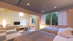 Een moderne hotelkamer met een groot bed, een bureau met stoel, een televisie en een groot raam met uitzicht op bomen.