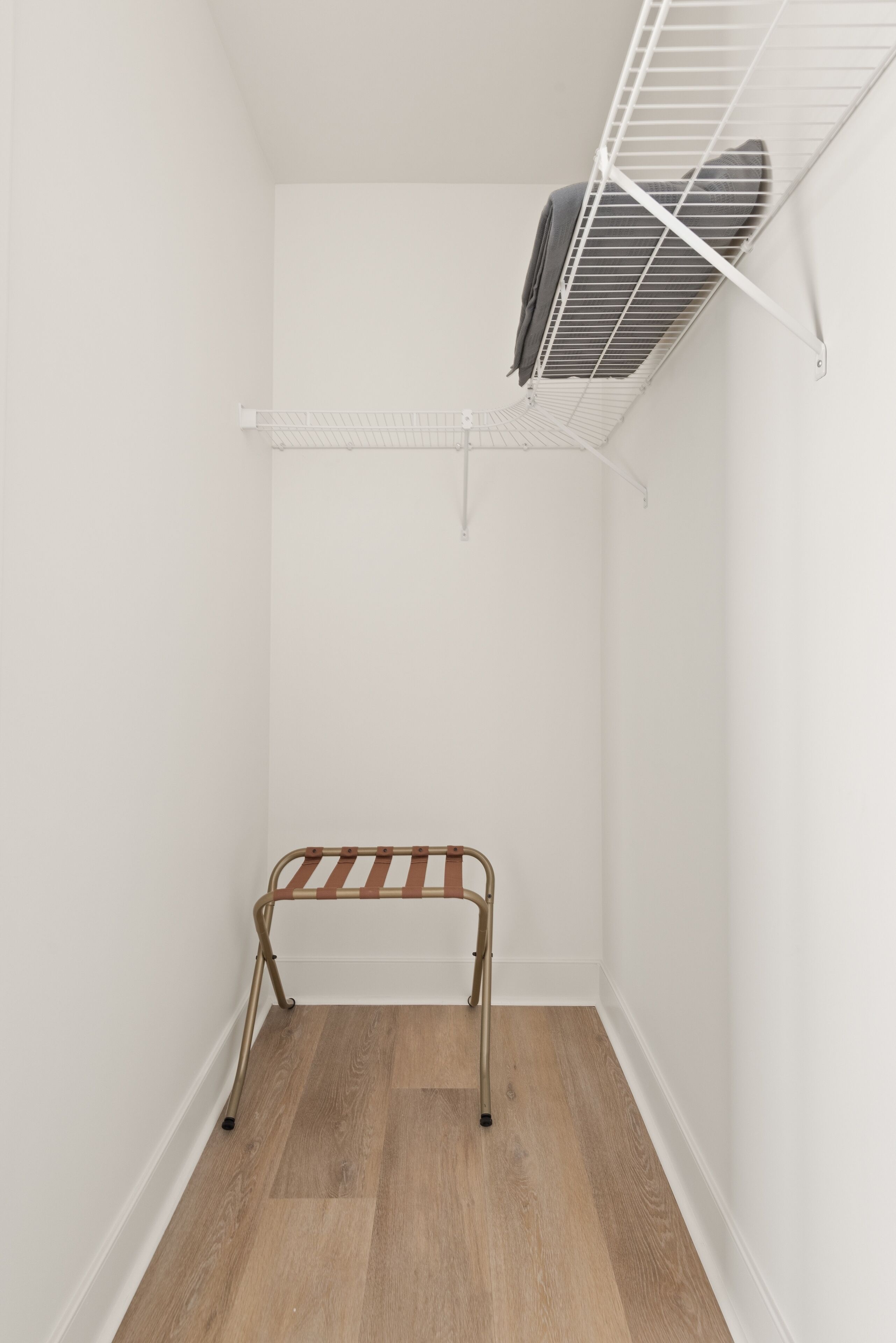 Een kleine, afgesloten ruimte met een houten bank, een witte muur en een metalen plankunit.