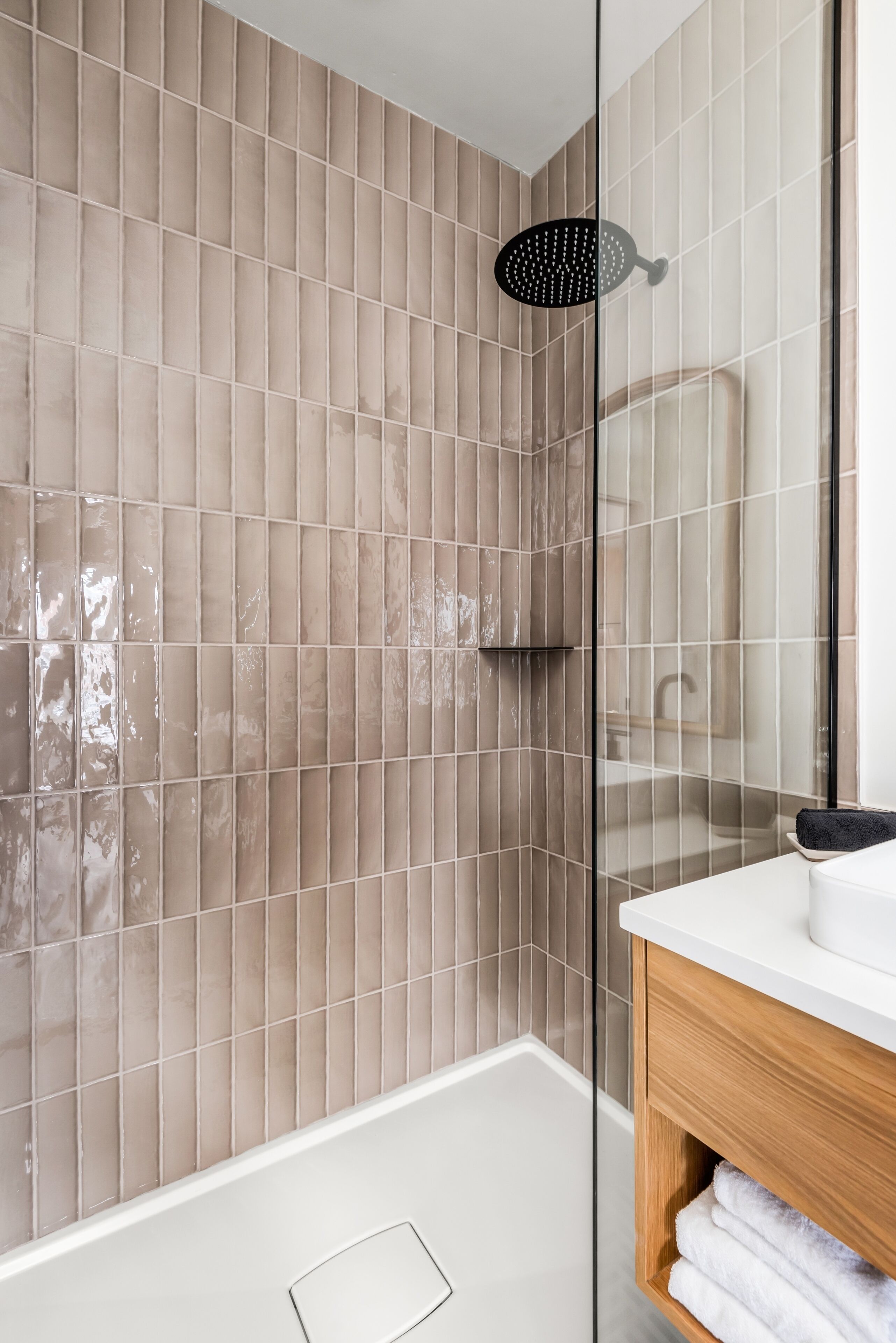 A modern bathroom with a glass shower enclosure, a wooden vanity, and a tiled wall.