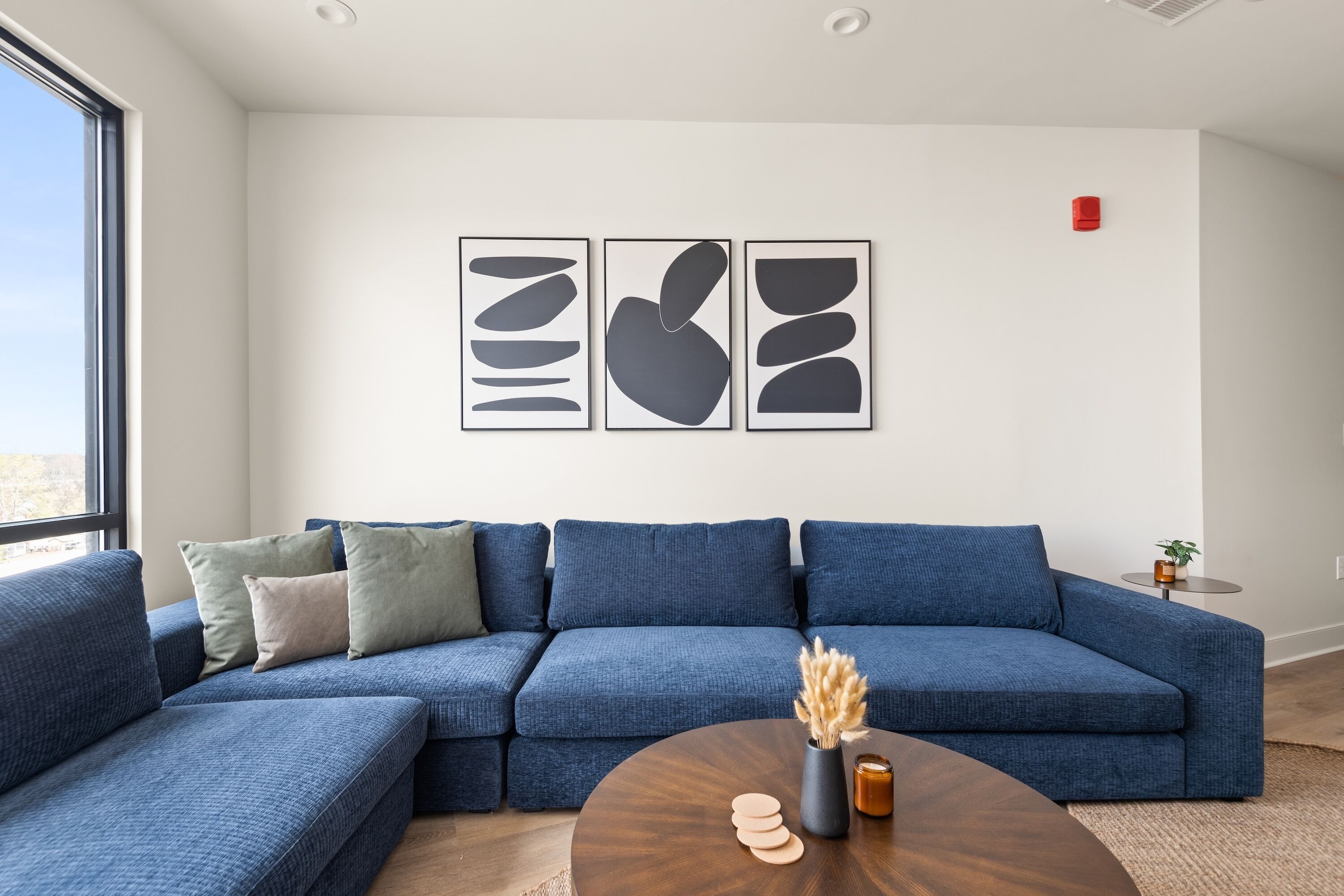 A modern living room with a blue sectional sofa, a round coffee table, and abstract wall art.