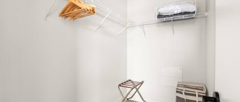 A compact room with a white wall, a wooden floor, a metal drying rack, a small storage unit, and a white ceiling.