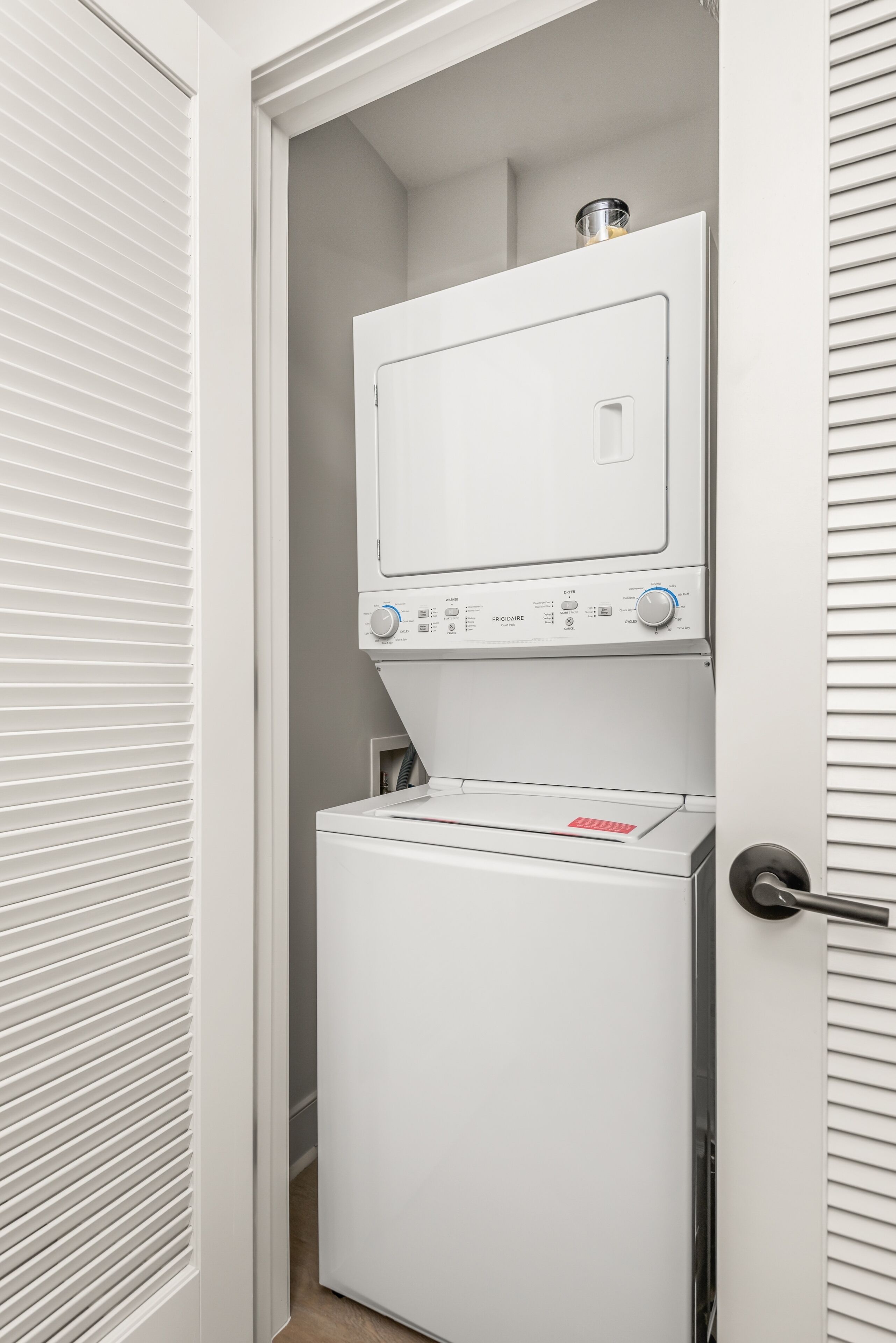 A compact laundry room with a front-loading washer and dryer, a small shelf above the dryer, and a door with a handle.