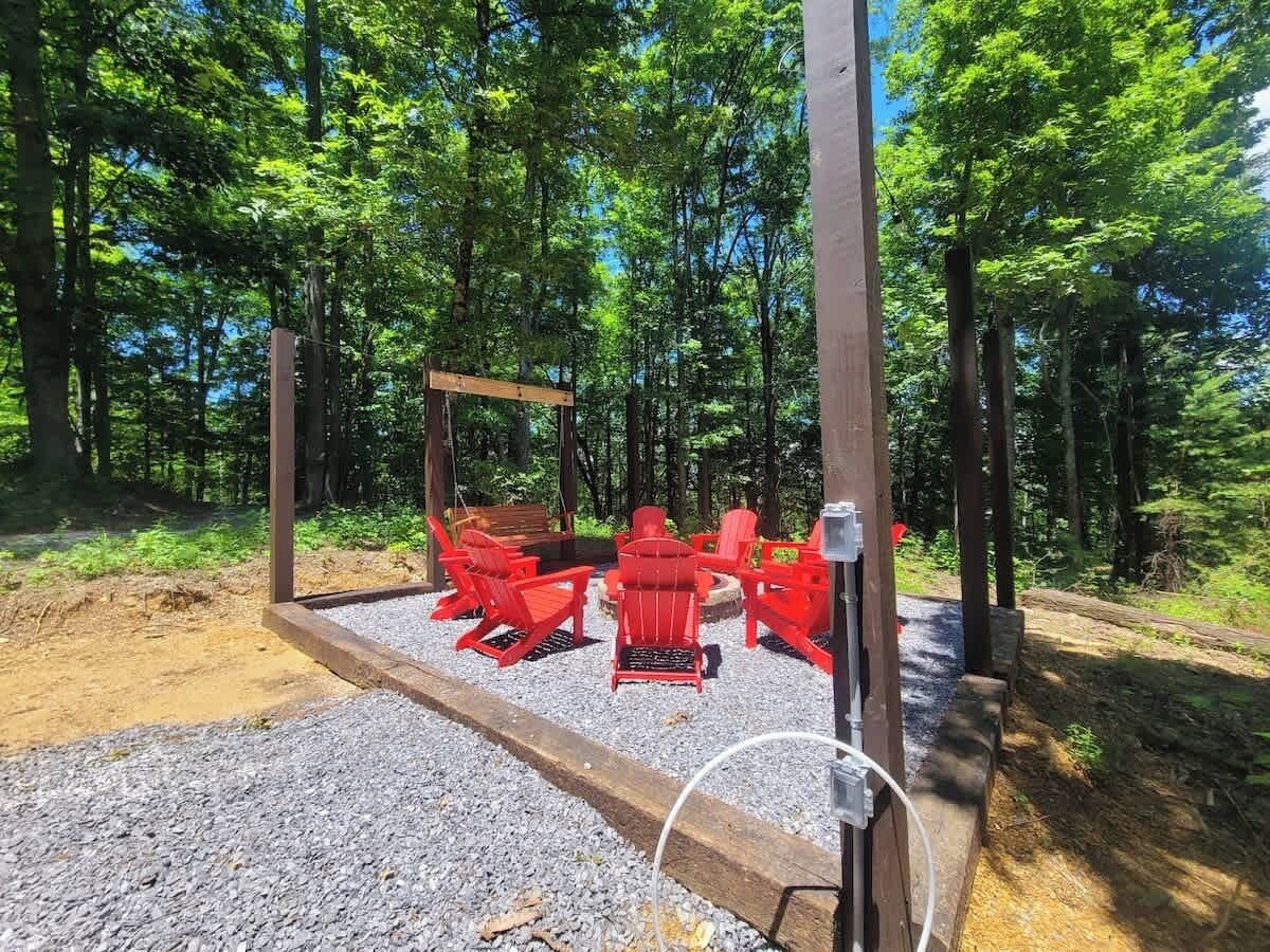 A forested area with a wooden deck and red Adirondack chairs.
