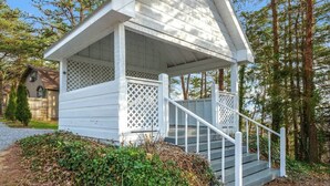 A small white wooden structure with a porch and stairs, surrounded by trees and a gravel path. - Nuthouse - Pickle Ball, Firepit, mountain views (Sevierville)
