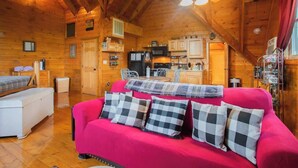 A cozy cabin interior with a wooden interior, a bright red sofa with checkered pillows, a ceiling fan, and a kitchen area with wooden cabinets and appliances. - Nuthouse - Pickle Ball, Firepit, mountain views (Sevierville)