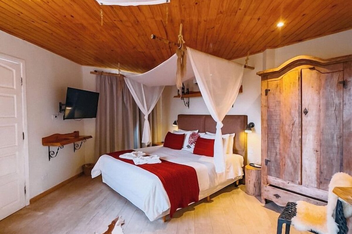 Ein Zimmer mit einem Bett, einer Holzbalkendecke, einem Kleiderschrank, einem Fernseher und einem Kuhfellteppich.