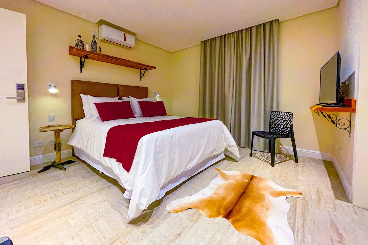 A hotel room with a bed, a chair, a mirror, a small table, and a fur rug.