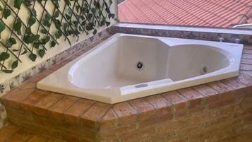Una bañera de spa con base de ladrillo, pared con diseño decorativo y vista a un tejado de tejas rojas.