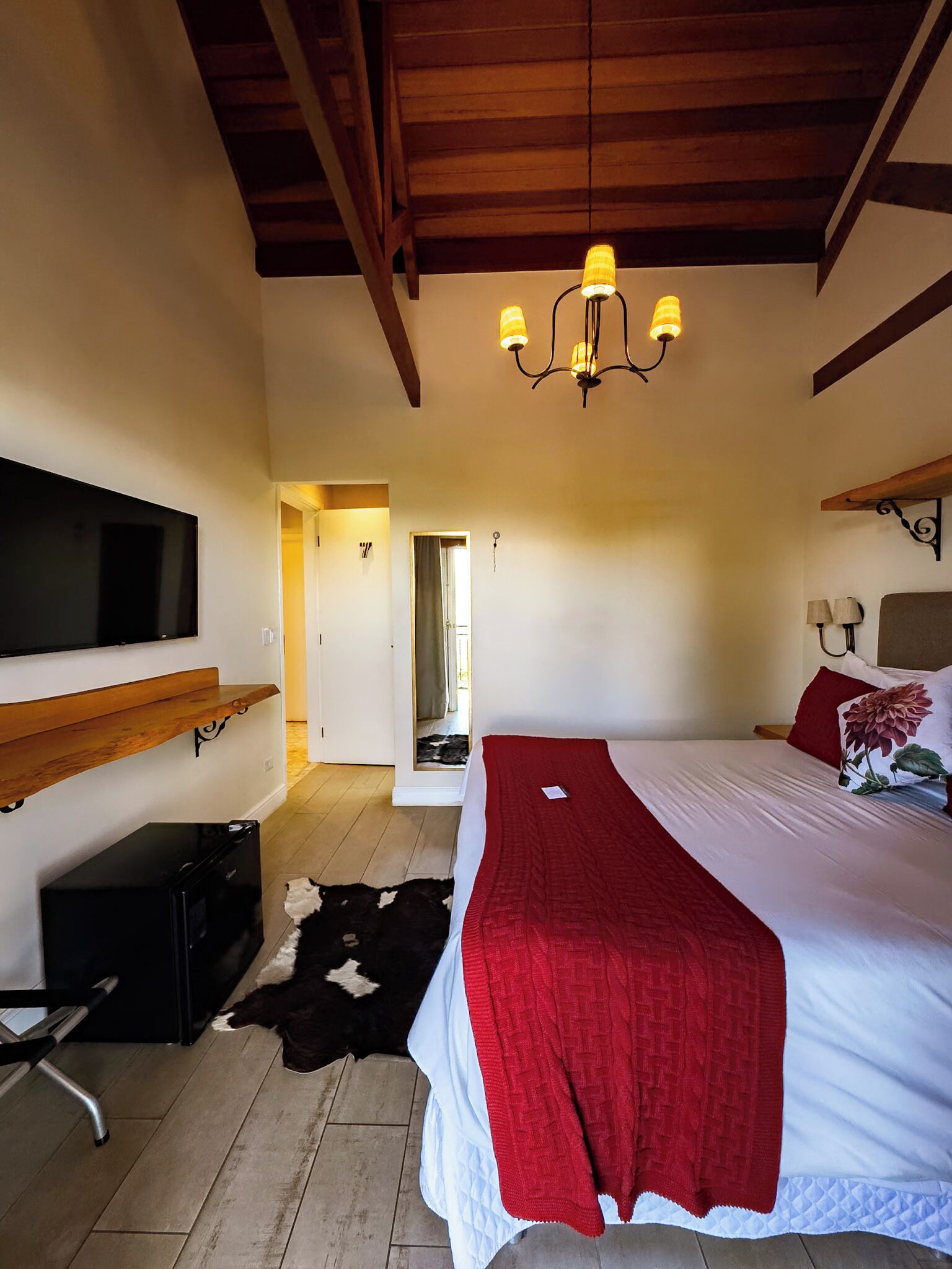 A bedroom with a bed, a TV, a desk, and a chandelier.
