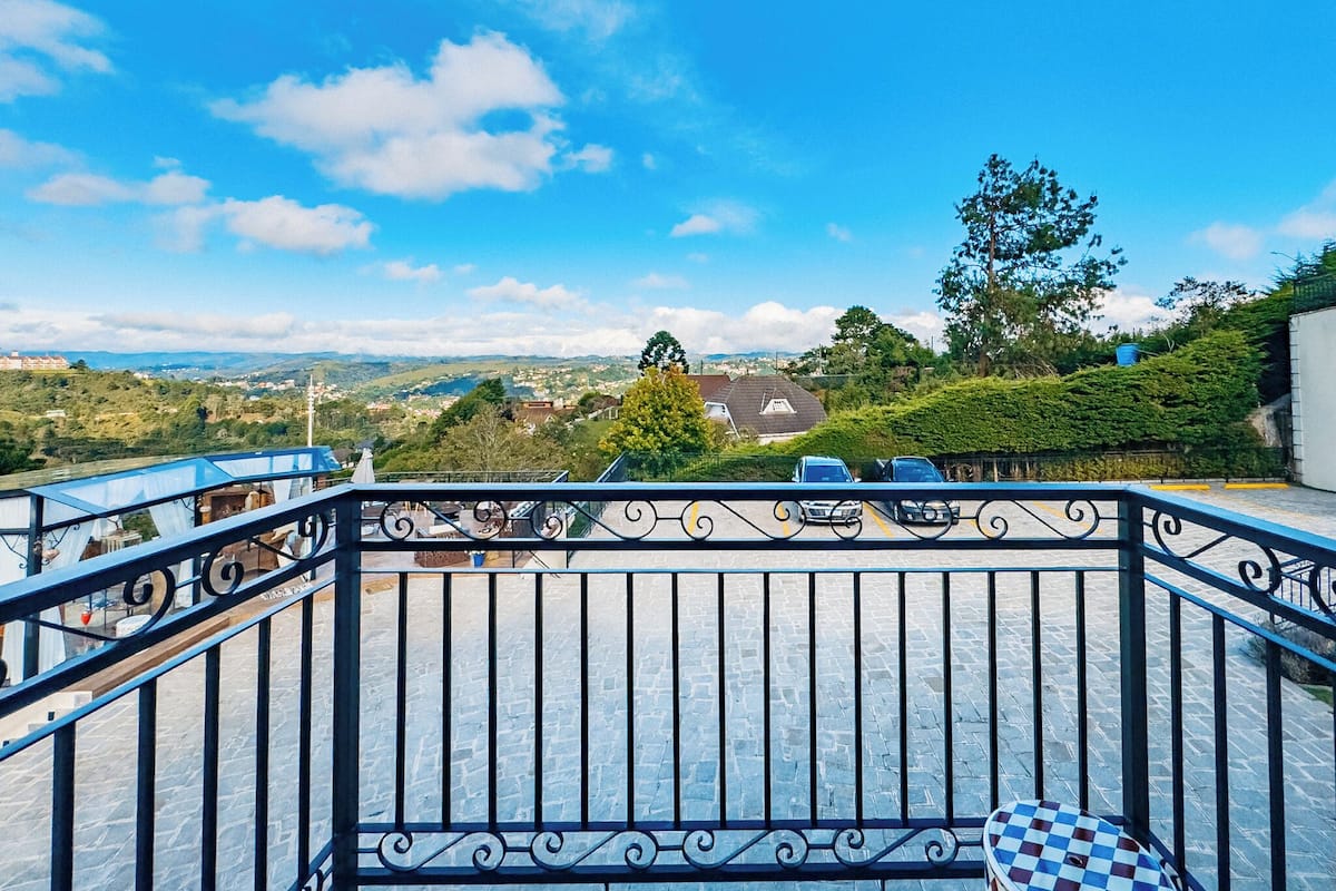 A balcony with a metal railing, a checkered table, and a view of a town with houses and trees.