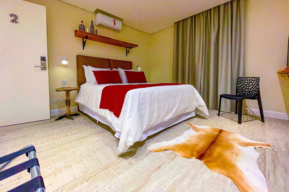 A hotel room with a bed, a chair, a rug, and a mounted air conditioner.