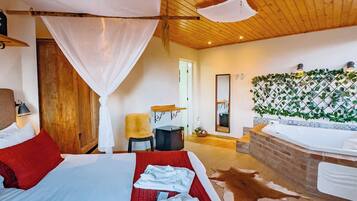 A bedroom with a large bed, a wooden ceiling, a small desk, and a bathroom with a bathtub.