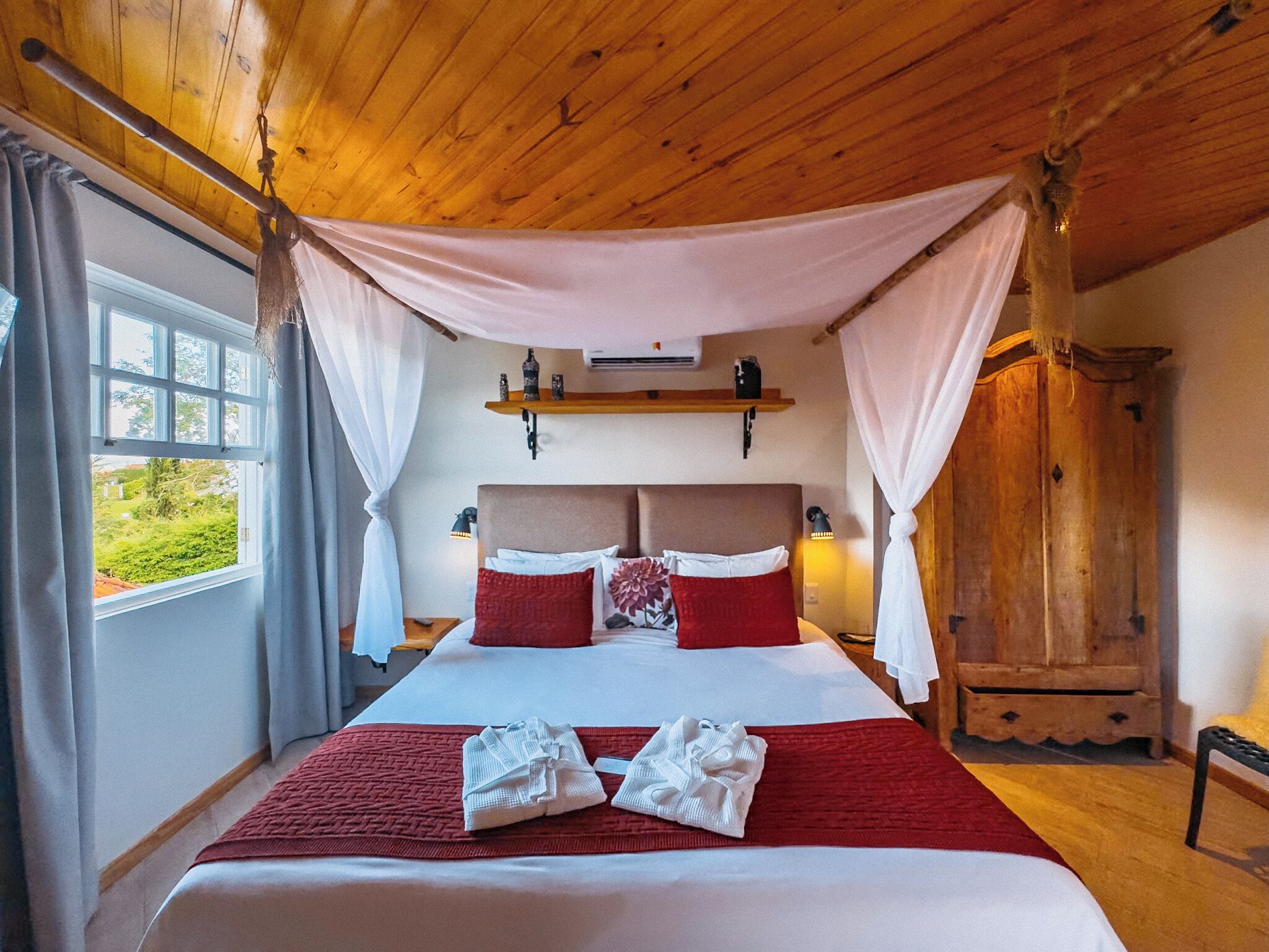 A large bed with a canopy, a wooden wardrobe, and a window with curtains.