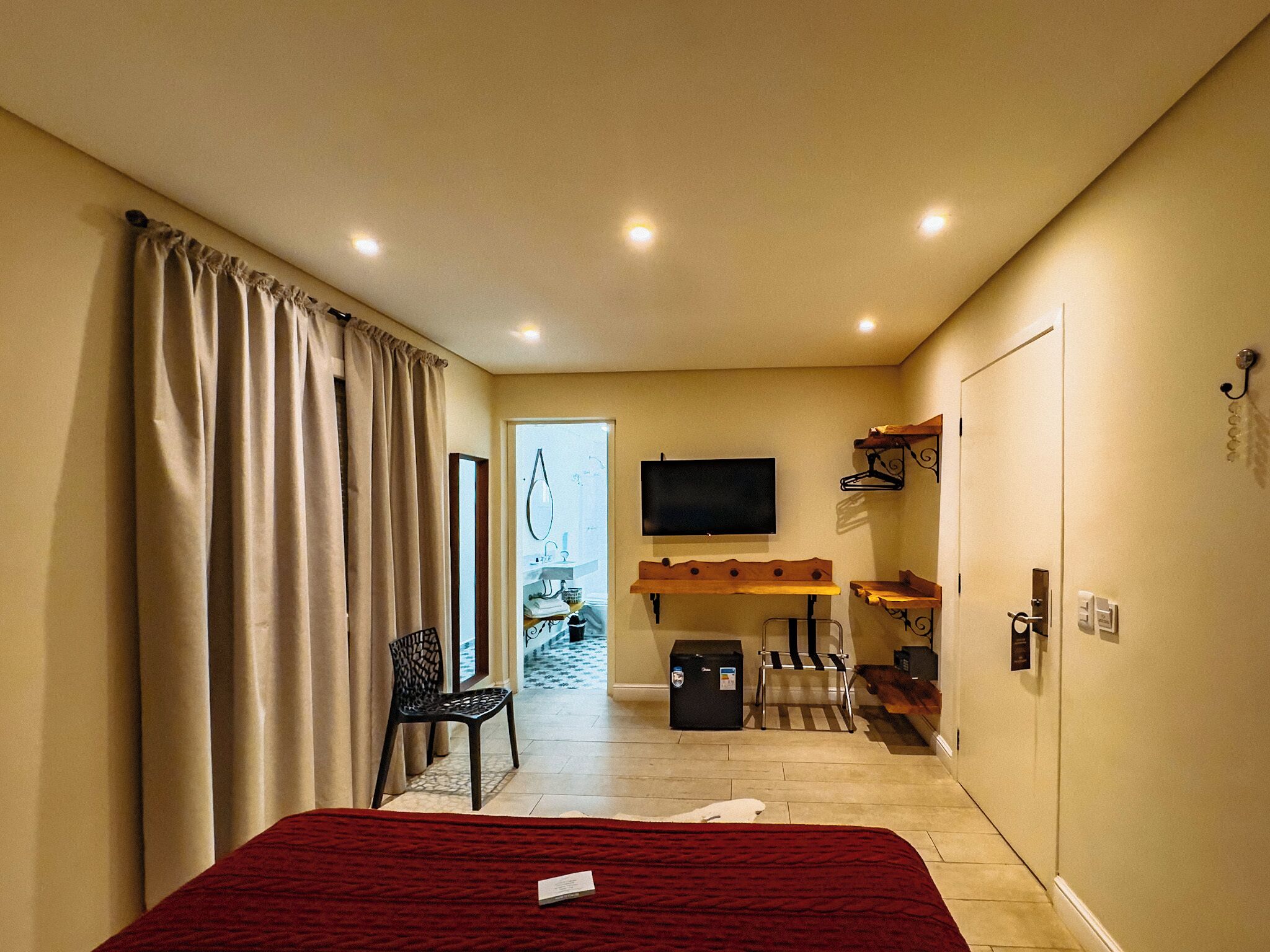 Een hotelkamer met een bed, een aan de muur bevestigde televisie, een bureau met een stoel, een kapstok en een koffer op de vloer.