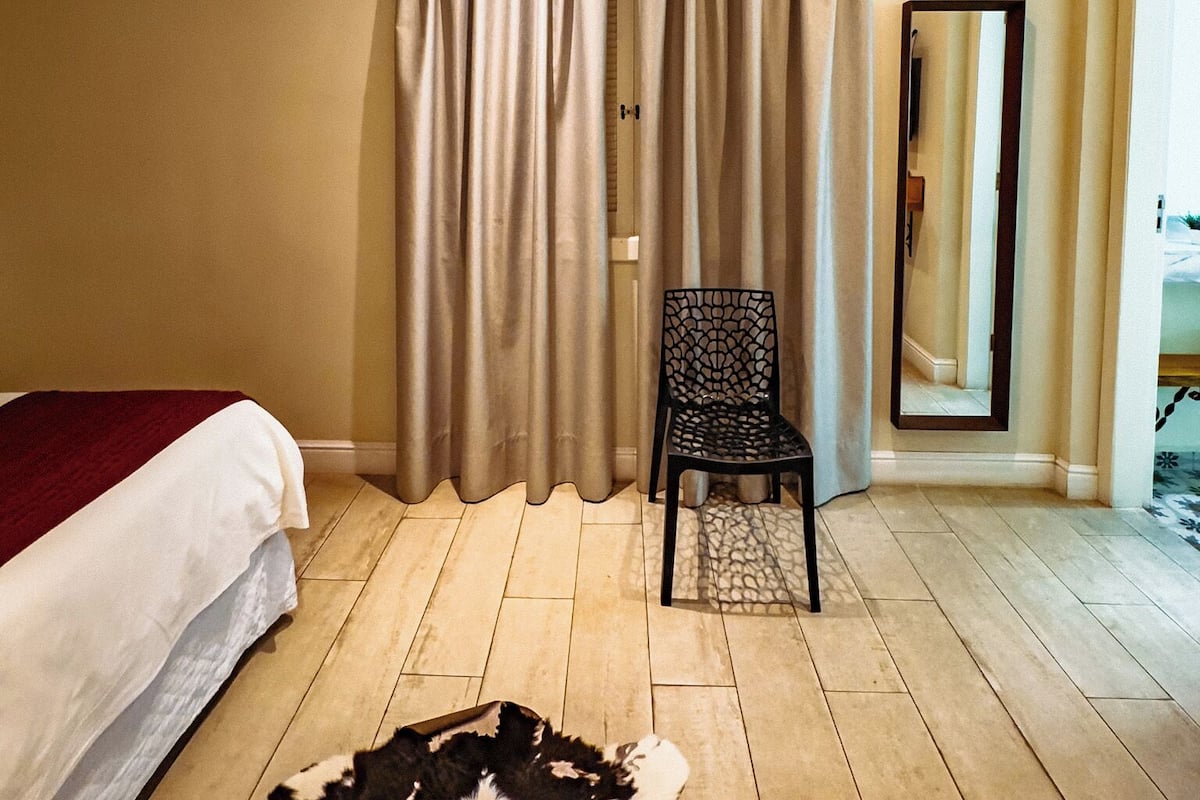 A hotel room with a bed, a chair, a mirror, and a rug.