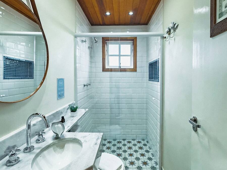 Baño con techo de madera, una ventana, lavabo, inodoro y baldosas de suelo con diseño.