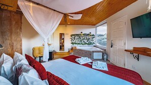 A bedroom with a large bed, a wooden ceiling, a window, a sink, and a TV.