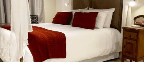 A bed with white bedding and red pillows, a wooden nightstand, and a wall-mounted light fixture.