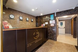 Un mostrador de recepción de hotel con relojes que muestran diferentes husos horarios, un mostrador con un logotipo y una zona de recepción con piso de mármol.