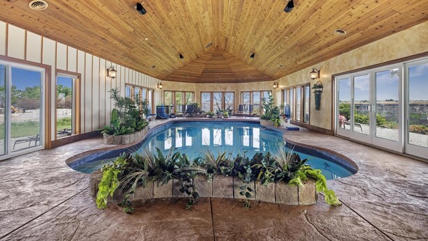 A spacious indoor pool area with a wooden ceiling, large windows, and potted plants around the pool. - Canyon Rim Retreat (Filer)