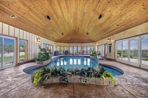 A spacious indoor pool area with a wooden ceiling, large windows, and potted plants around the pool. - Canyon Rim Retreat (Filer)