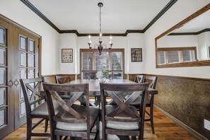 A dining room with a round table, dark wooden chairs, a chandelier, and wooden paneling on the walls. - Canyon Rim Retreat (Filer)