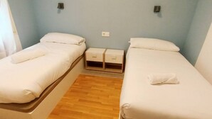 Ein Doppelzimmer mit zwei Einzelbetten, einem kleinen Nachttisch mit Schubladen und einer hellblauen Wand.
