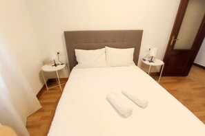 A hotel room with a large bed, two bedside tables with lamps, and a wooden floor.