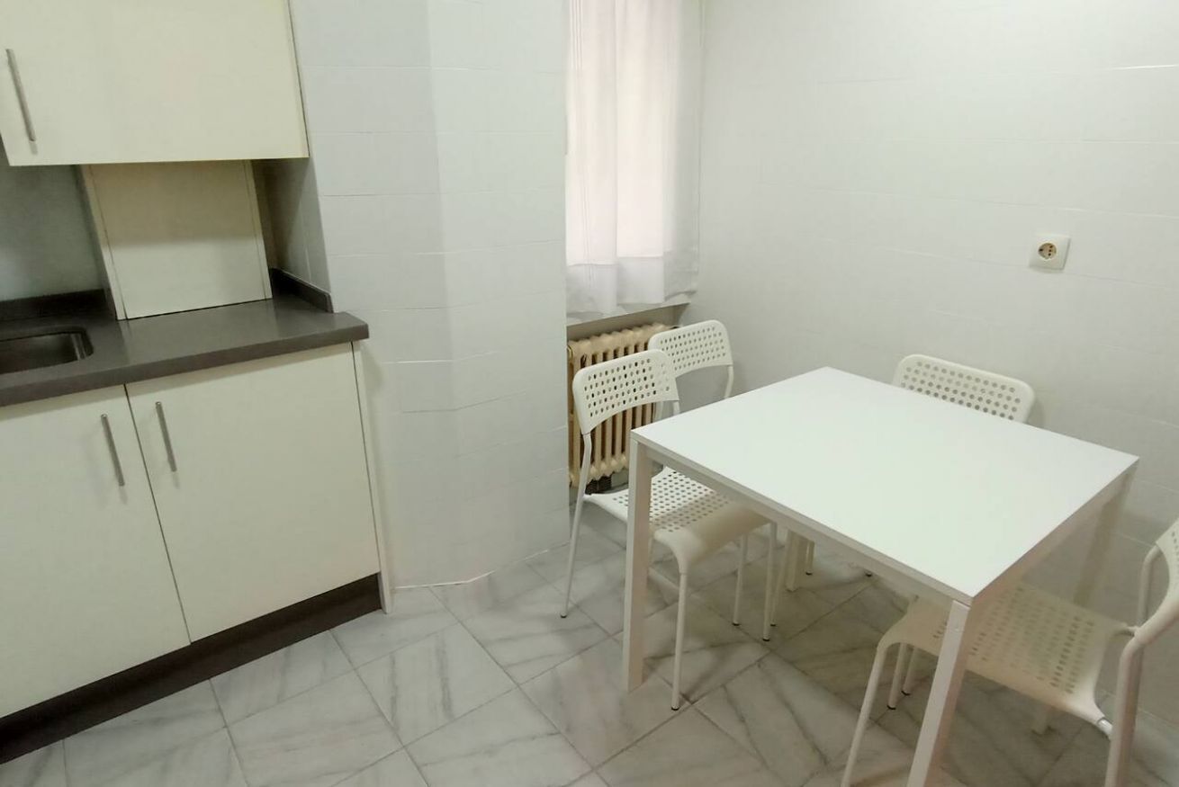 A small kitchen with white cabinets, a white table, and two white chairs.