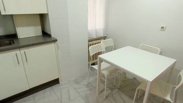 A small kitchen with white cabinets, a white table, and two white chairs.