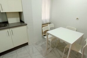 Een kleine keuken met witte kastjes, een witte tafel en twee witte stoelen.