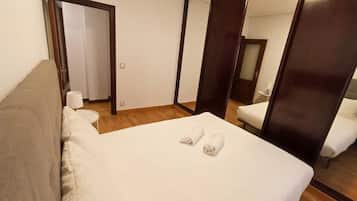 A hotel room with a bed, a sofa, a small table, a mirror, and a door.