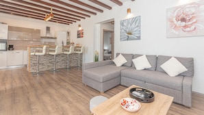 Un salon moderne avec un canapé d’angle gris, une table basse en bois et une cuisine en arrière-plan.