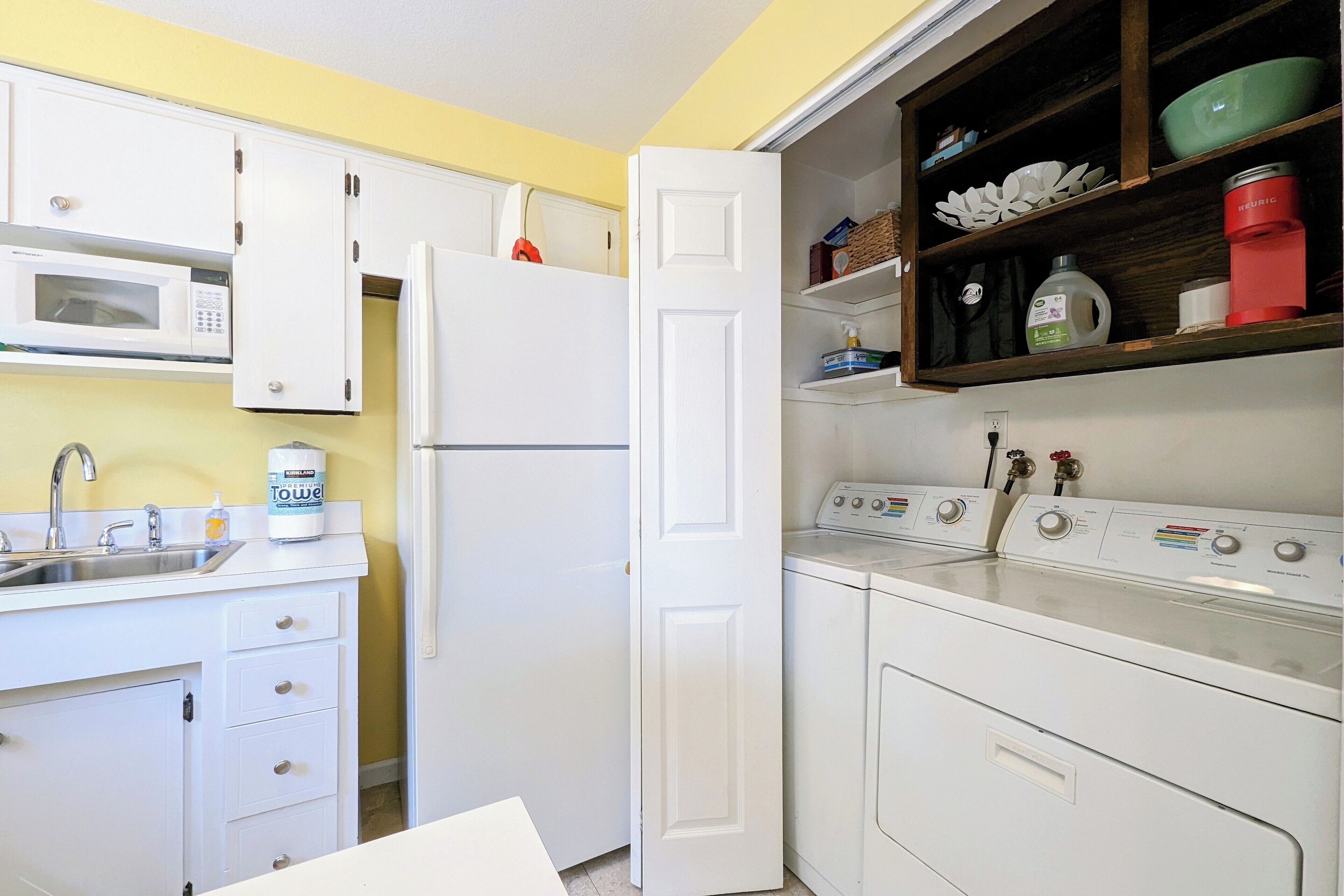 A compact kitchen with white cabinets, a microwave, a refrigerator, a sink, and a built-in washer and dryer.