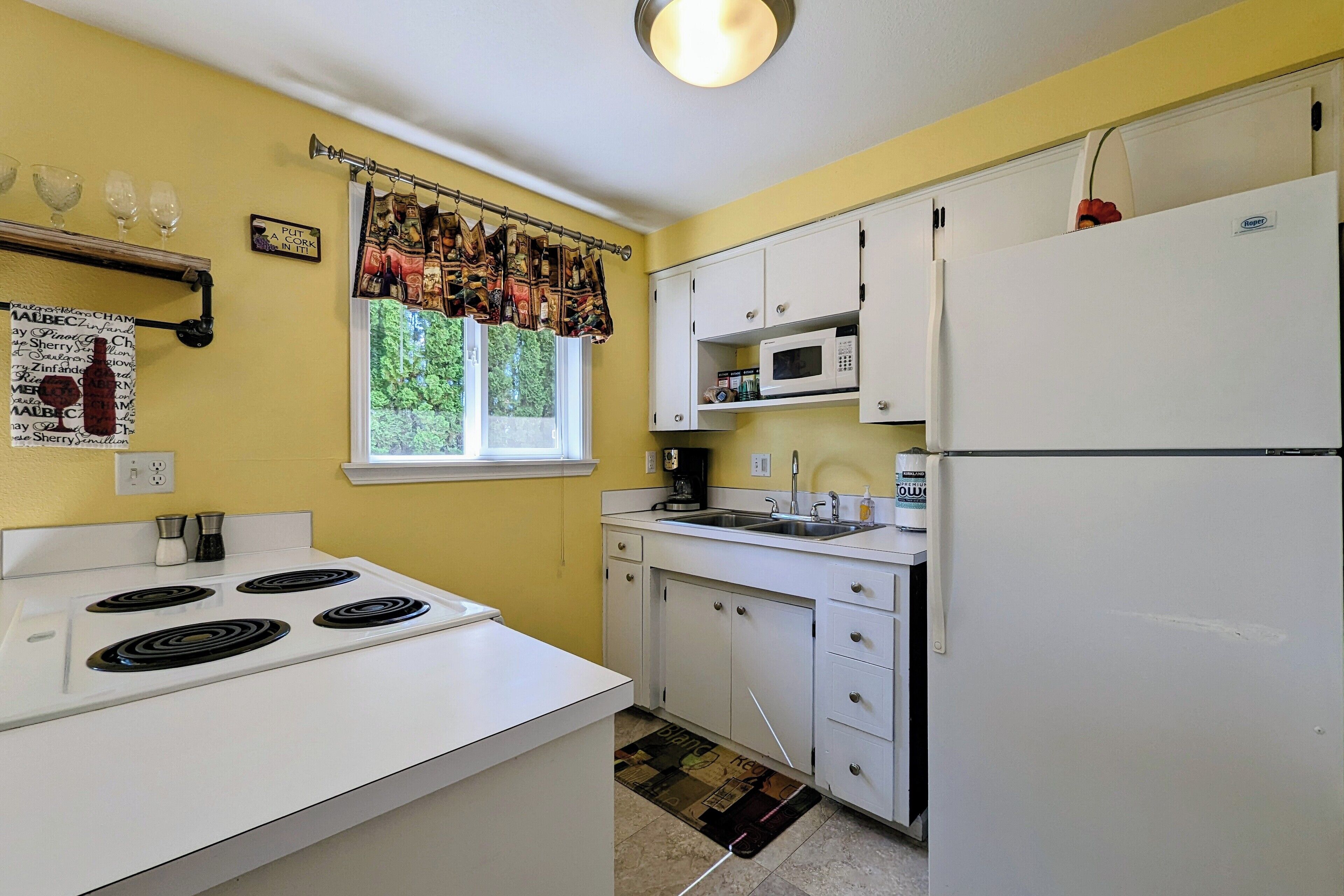 A kitchen with white cabinets, a stove, a refrigerator, and a window with a curtain.