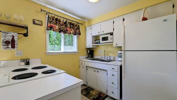 A kitchen with white cabinets, a stove, a refrigerator, and a window with a curtain.