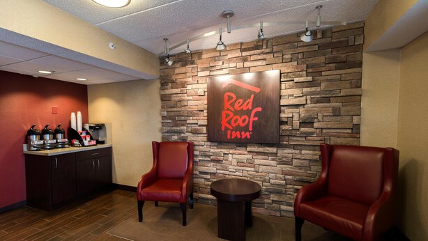 Un hall d’entrée d’un Red Roof Inn avec un mur en pierre, deux fauteuils en cuir, une petite table et un coin café.